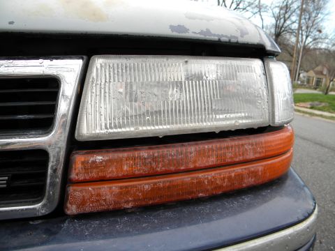 1993 Dodge Grand Caravan - Close-up of a worn minivan's front corner, revealing a clear headlight and amber turn signal.