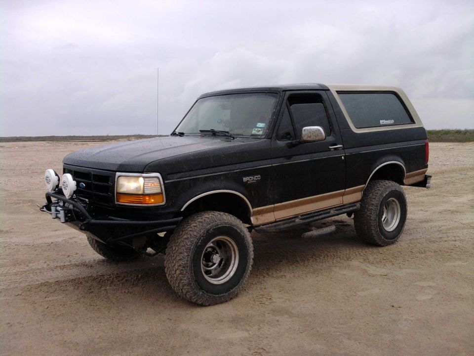 Black Ford Bronco with tan trim and aftermarket bumper with lights, parked on sand
