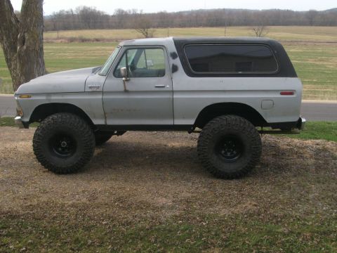 1979 Ford Bronco - This lifted 1979 Ford Bronco features a two-tone paint scheme with a gray body and black hardtop, complemented by aggressive off-road tires.
