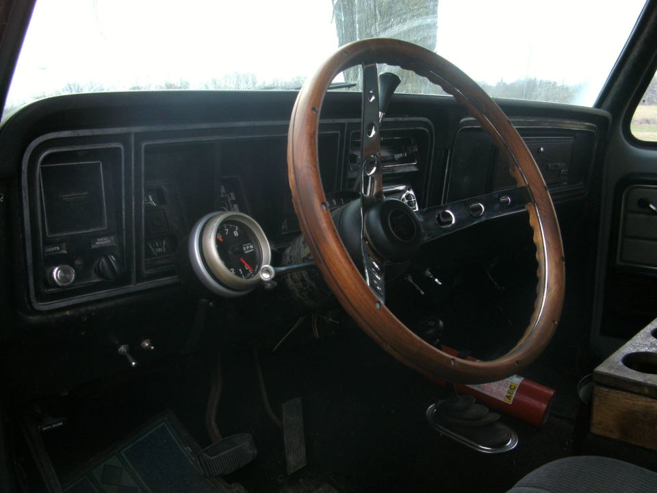 Dashboard and wooden steering wheel of a vehicle, with an aftermarket gauge mounted to the dash