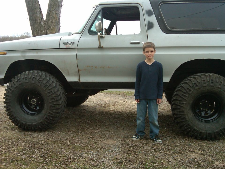 Gray Ford Bronco with large tires, side view, boy standing next to it