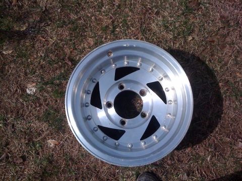 1995 Ford Bronco - A single aluminum wheel with a distinctive five-spoke design rests on a patch of dry grass.