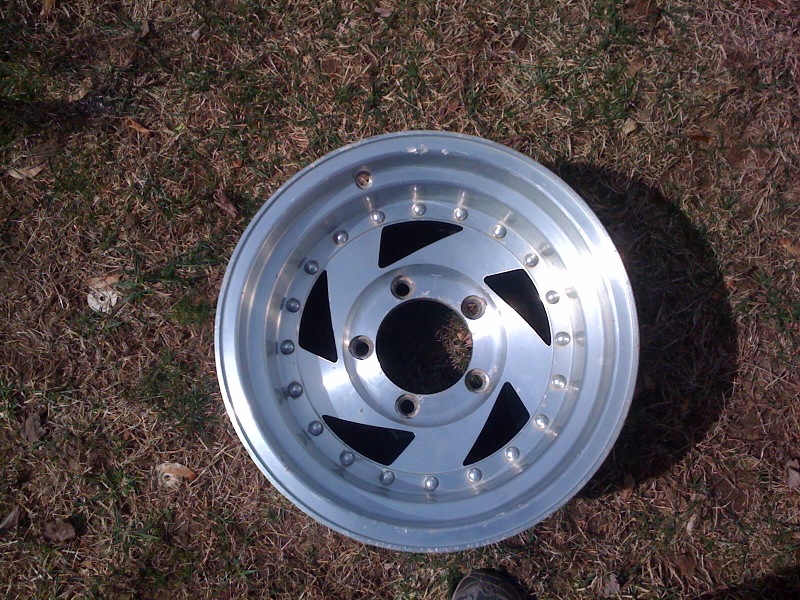 Aluminum alloy wheel with five triangular cutouts and a polished lip, lying on grass