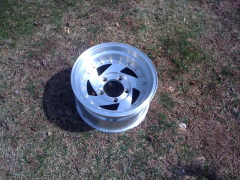 1995 Ford Bronco - A single aluminum wheel with a distinctive spoke pattern is shown on a grassy surface.
