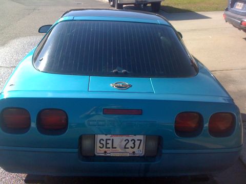 1995 Ford Bronco - The rear of a teal Corvette shows its distinctive taillights and the 'Corvette' script across the trunk lid.