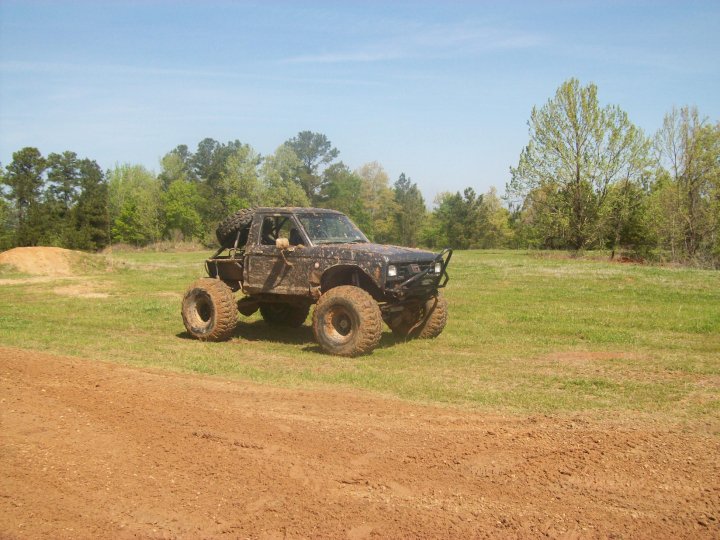 Muddy off-road SUV with oversized tires and spare tire on back, parked in a grassy field