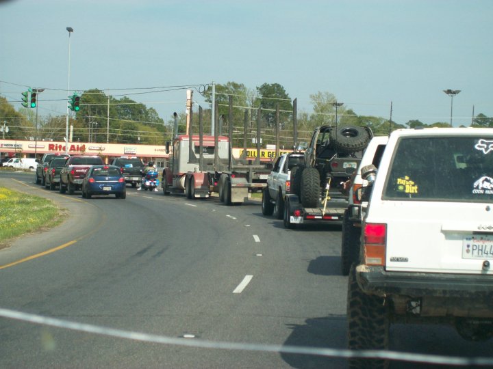 Traffic jam on a road with a logging truck, a trailer with an off-road vehicle, and other cars