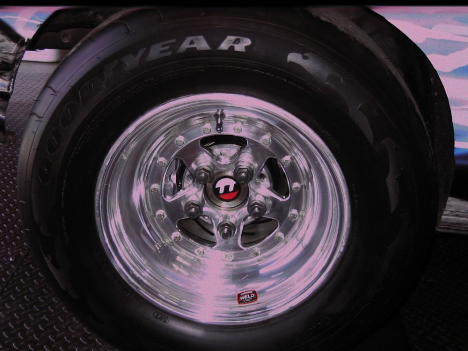 Close-up of a polished Weld racing wheel with a Goodyear tire, showing a red and black center cap and a "WELD" sticker