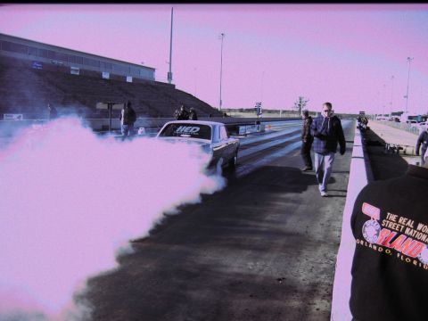 1992 Ford Mustang - A classic Ford Mustang performs a burnout on the drag strip, creating a cloud of pink smoke.