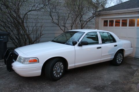 2003 Ford Crown Victoria - A white 2003 Ford Crown Victoria is parked in front of a garage, showing its front push bumper.
