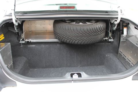 2003 Ford Crown Victoria - The trunk of a car shows a spare tire and some custom metal storage compartments.