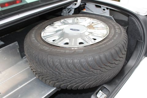 2003 Ford Crown Victoria - A spare tire rests in the trunk of a vehicle, showing a Ford logo on its hubcap.