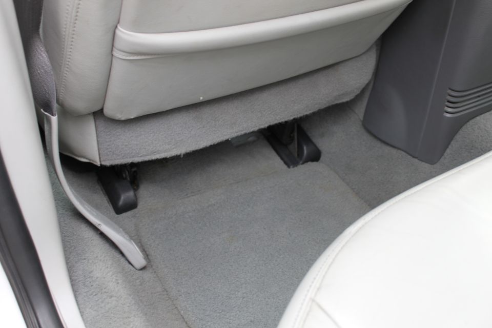 Car interior floor with gray carpet and light gray seats. Shows seat rails and part of a center console