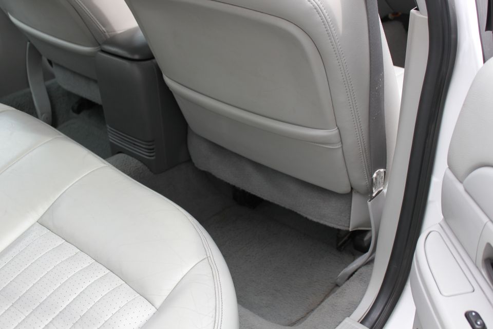 Car interior showing light gray leather seats, a dark gray center console, and a seatbelt. Watermark "SUPERMOTORS" is visible