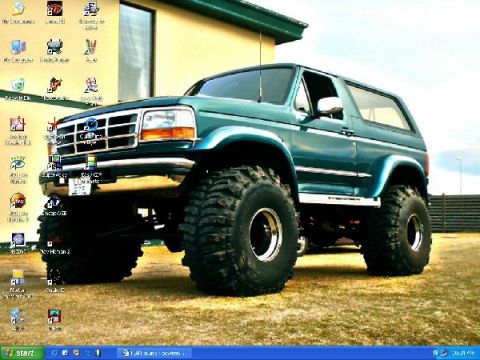 1995 Ford Bronco - A teal Ford Bronco with large off-road tires and a lifted suspension sits on a grassy area.