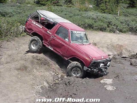 2002 Ford F-350 - This red off-road truck appears to be stuck in the mud, with a spare tire mounted on the rear and a tarp covering the bed.