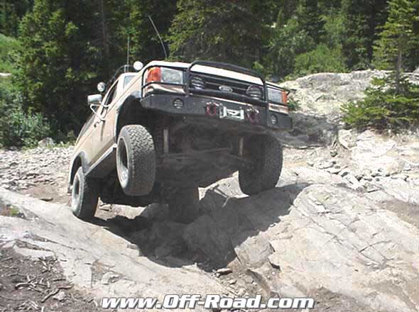 Tan lifted Ford truck with black brush guard and driving lights crawling over a granite slab