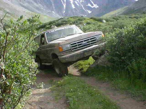 2002 Ford F-350 - A brown Ford Bronco navigates a rocky trail in a mountainous, green landscape.