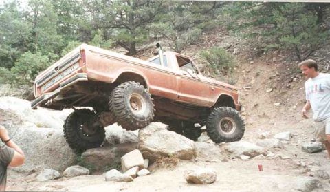 2002 Ford F-350 - A man watches as a modified pickup truck drives over large rocks on a trail.