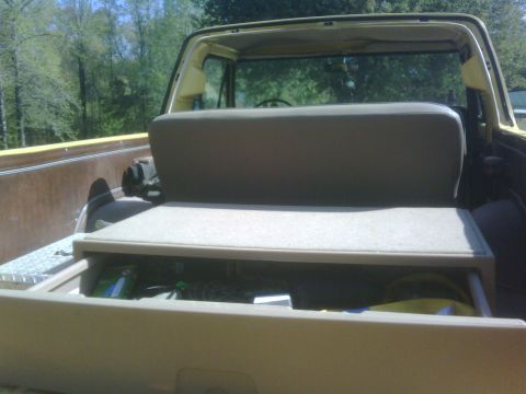 1978 Ford Bronco - The rear cargo area of a yellow 1978 Ford Bronco shows a folded-down seat and an open storage drawer.