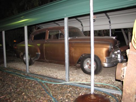 1984 Ford Bronco - A vintage sedan with a metallic brown finish sits under a green-roofed carport.