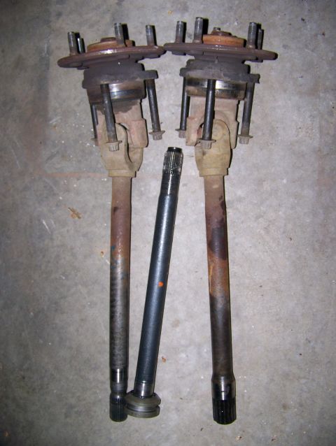 2001 Dodge 1500 - Three automotive driveshafts, two with attached hubs, lie on a concrete surface.