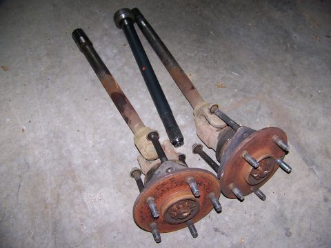 2001 Dodge 1500 - Two rusty axle shafts with hubs and a black shaft are displayed on a concrete surface, with a SuperMotors watermark visible.