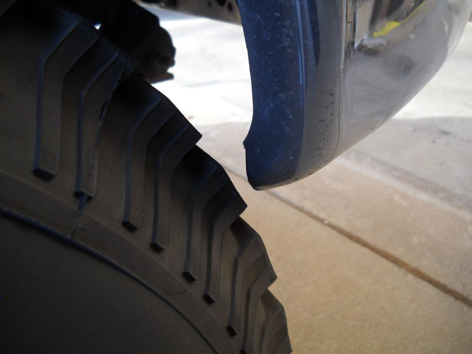 Close-up of a large tire tread and a dark blue fender flare with a small chip