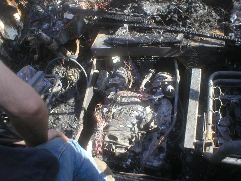 1998 GMC Sierra 3500 - The aftermath of a fire shows a severely damaged engine compartment with charred components and exposed wiring.