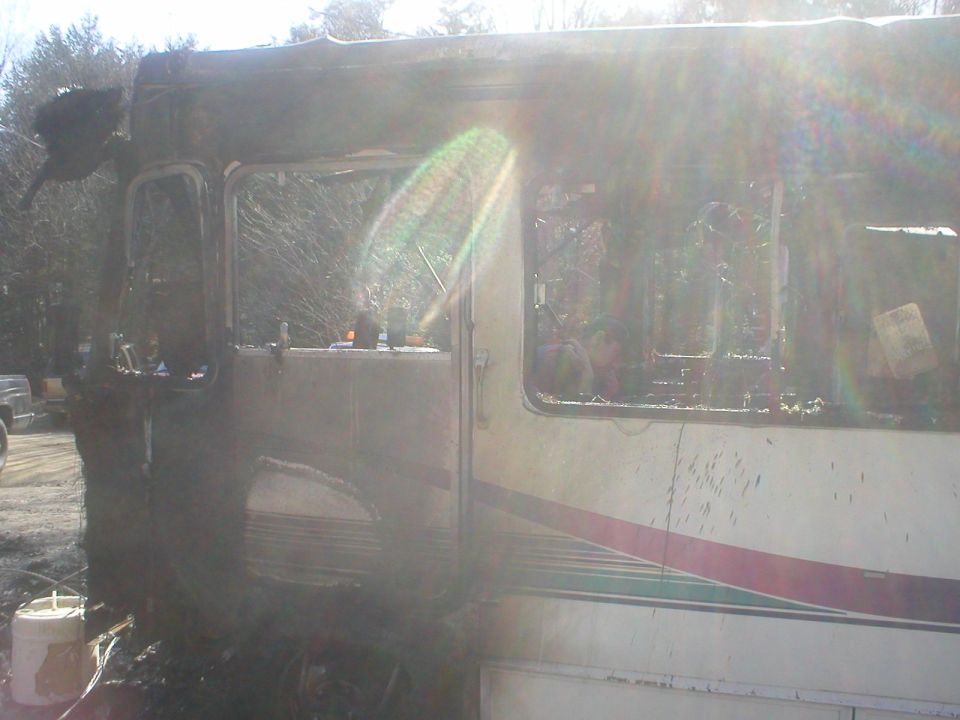 Side view of a burnt RV with windows shattered and interior charred