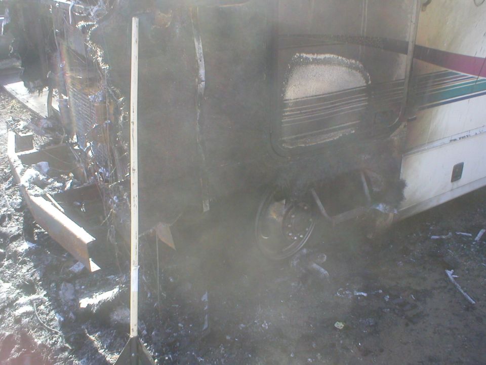 Burnt-out RV side view with melted siding and visible wheel