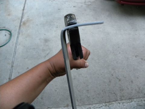 1995 Ford Bronco - A hand uses a hammer to bend a metal rod, with a portion of a red vehicle visible in the background.
