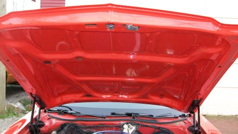 1973 Ford Ranchero - The underside of a red car's hood is shown, revealing structural supports and the area beneath.
