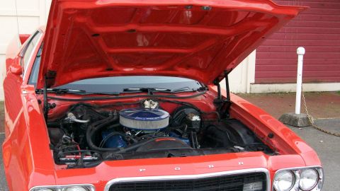 1973 Ford Ranchero - The engine bay of a red 1973 Ford Ranchero is visible with the hood raised.