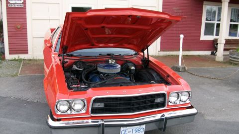1973 Ford Ranchero - The engine bay of a red vehicle is open, revealing the blue engine and air filter. The license plate indicates the year 1983.
