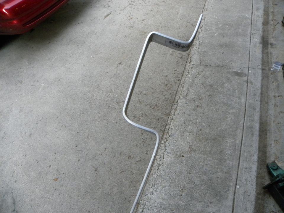 metal bar with a sticker on it, lying on concrete floor next to a red car part
