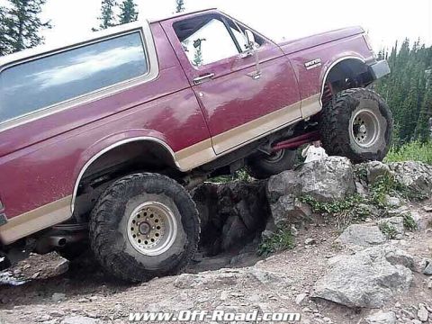 2002 Ford F-350 - This lifted Ford Bronco is navigating a rocky off-road trail with a person visible behind the front tire.