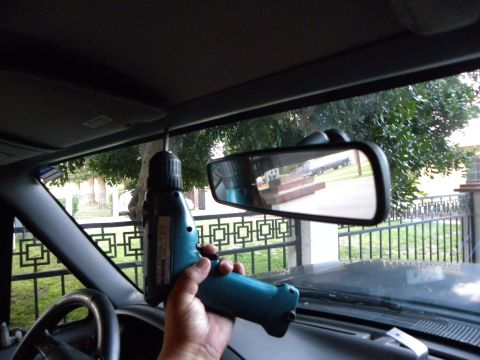 1995 Ford Bronco - A drill is used inside a vehicle, with the rearview mirror reflecting a truck outside.