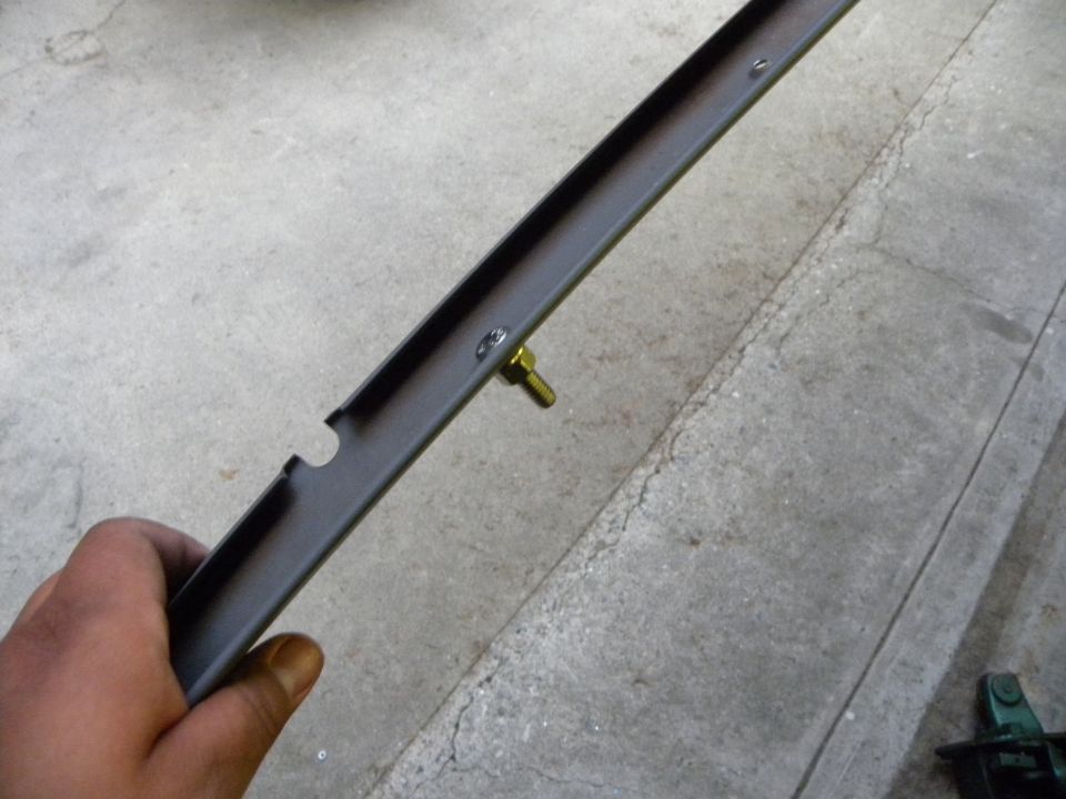 Hand holding dark metal bracket with a brass bolt attached