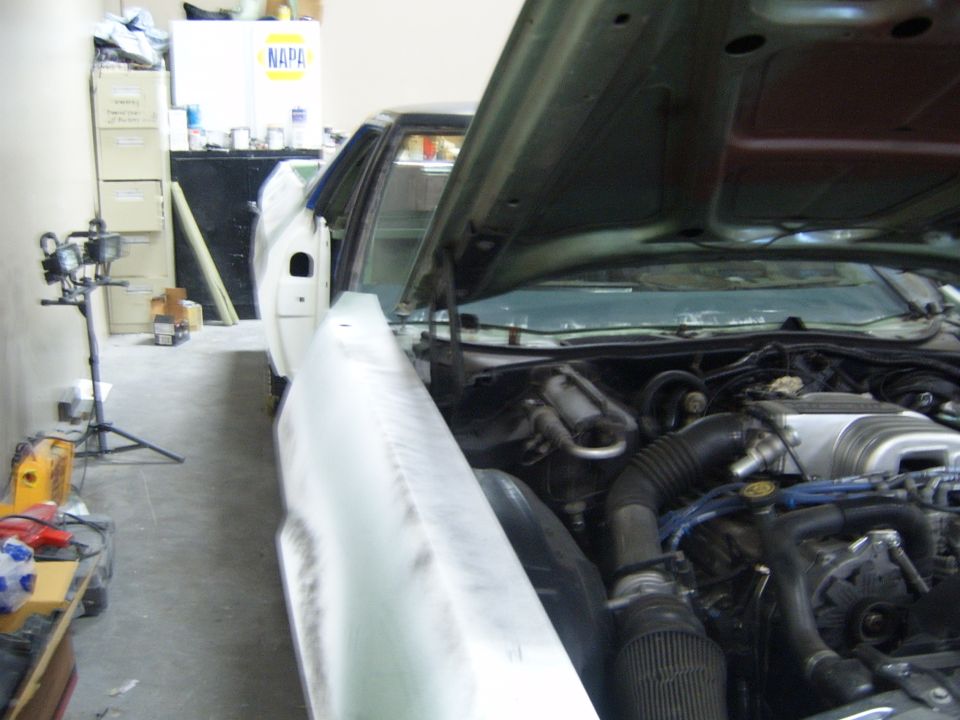 Car in garage with hood open showing engine and fender. Some bodywork appears to be in progress