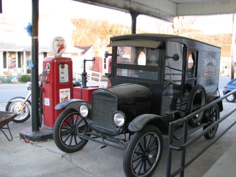 2006 Victory Kingpin - A vintage truck with a boxy rear compartment is parked next to an old gas pump, with a motorcycle visible to the left.