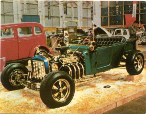 1969 Lincoln Continental - A custom green hot rod is displayed indoors next to a red sedan, with spectators in the background.