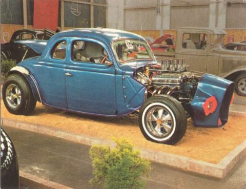 1969 Lincoln Continental - A custom blue hot rod coupe is displayed with its engine prominently visible, alongside other vehicles in the background.