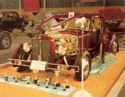 1969 Lincoln Continental - A maroon hot rod coupe is displayed with its engine exposed and surrounded by trophies, suggesting it's at a car show.