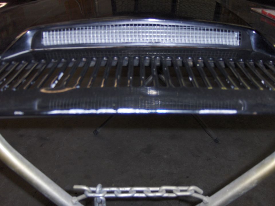 Black car grille with horizontal bars and a rectangular mesh vent above. Some white paint marks on the grille