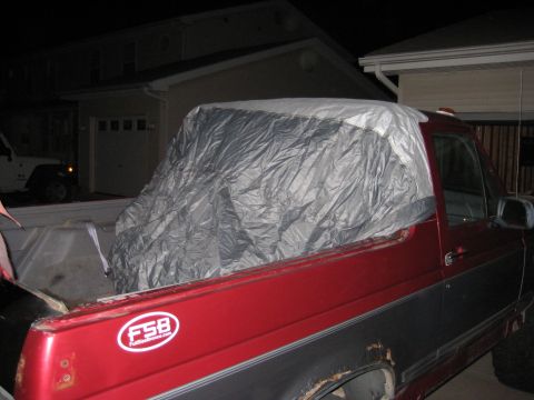 1995 Ford Bronco - A red pickup truck has its bed covered with a silver tarp. A white Jeep is visible in the background.