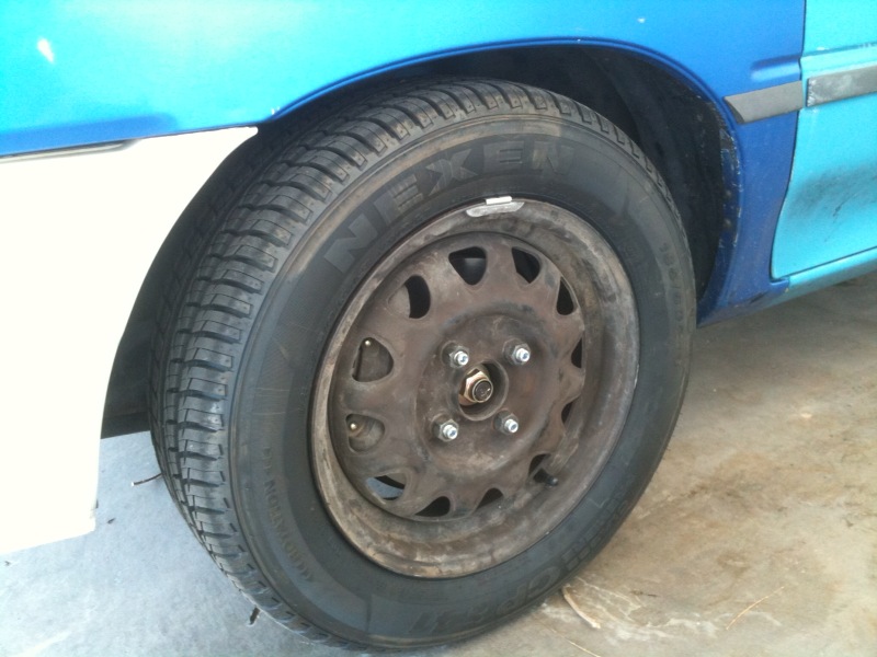 Bare steel wheel with Nexen tire on a blue hatchback, hubcap removed in a garage