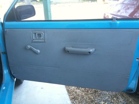 1991 Ford Festiva - Close-up of a blue car's interior door panel, showing the manual window crank and door handle.