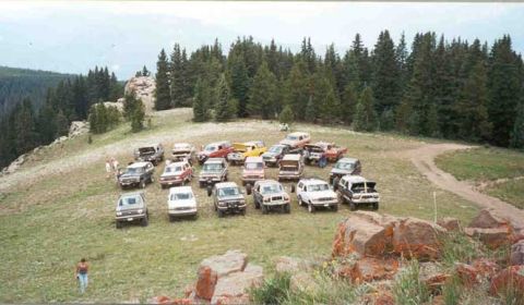 2002 Ford F-350 - Many SUVs and trucks are parked on a hill, with a forest behind them.