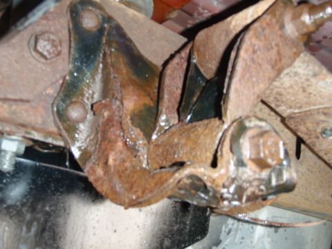 1995 Ford Bronco - This heavily corroded metal bracket is a component of a vehicle's undercarriage, likely part of the suspension system.